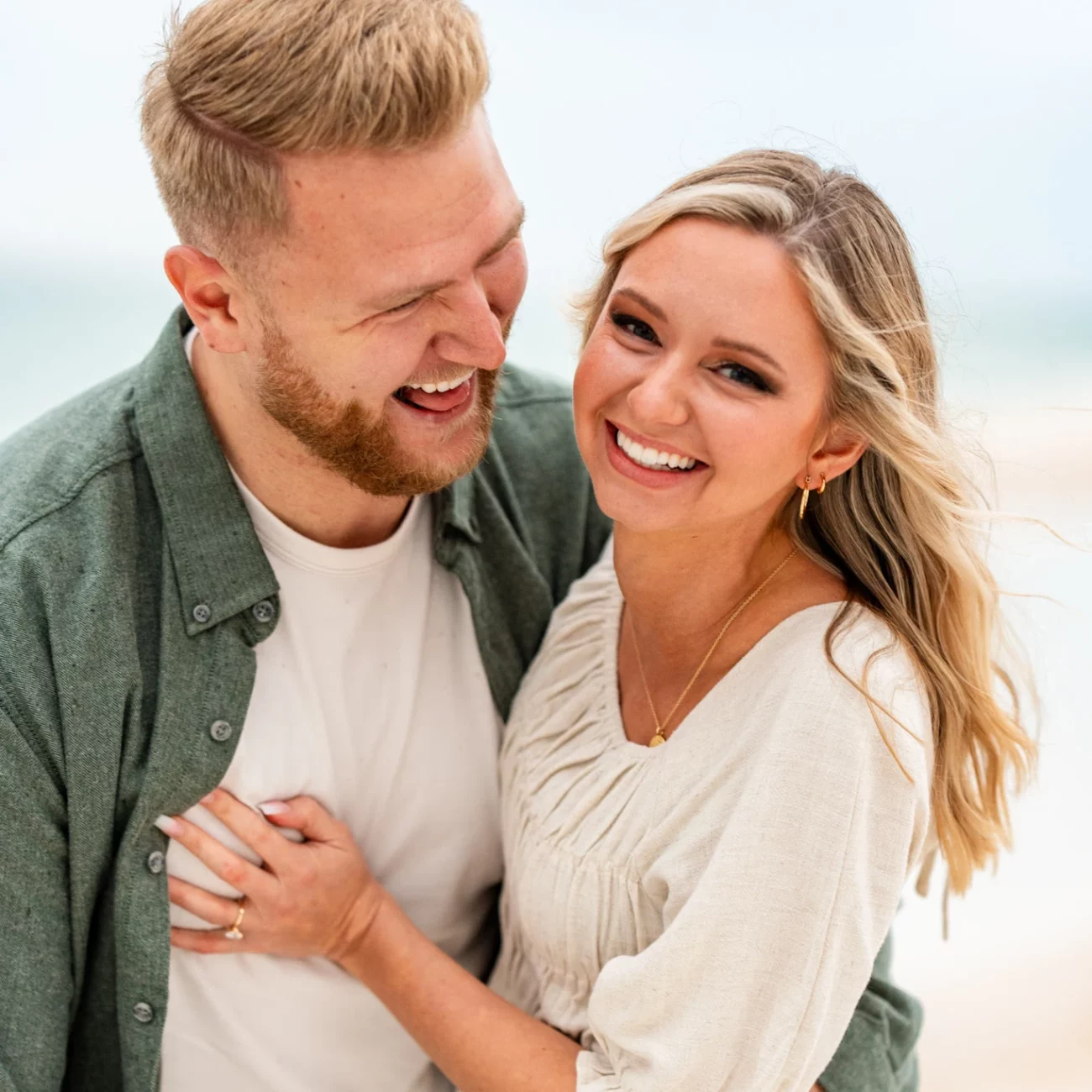 a man and woman smiling at each other on Pensacola Beach during their Engagement Photo Shoot by KDH Weddings