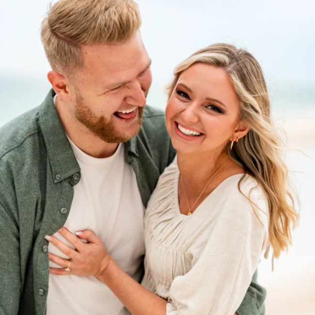 a man and woman smiling at each other on Pensacola Beach during their Engagement Photo Shoot by KDH Weddings
