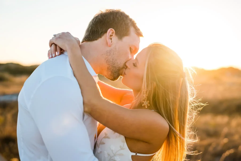 Beach Engagement Photos on the Gulf Coast: Spots, Timing and What to Wear 1 Ryan and Kinsie kissing in the Fort Pickens dunes, backlit by the setting sun over the sea oats