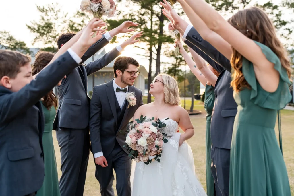 husband and wife walking under arch of groomsmen and bridesmaids hands