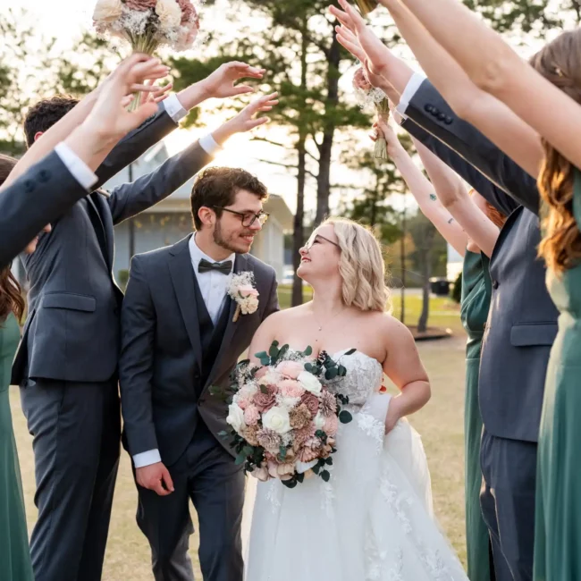 husband and wife walking under arch of groomsmen and bridesmaids hands
