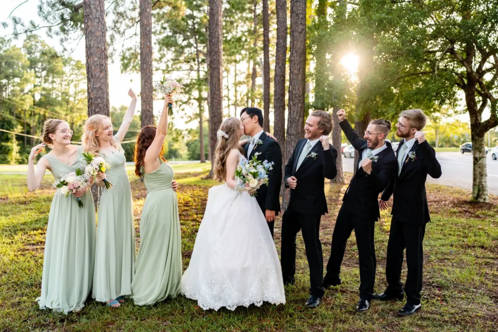 husband and wife kissing with groomsmen and bridesmaids on each side in a forst