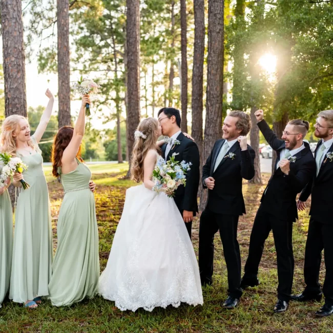 husband and wife kissing with groomsmen and bridesmaids on each side in a forst