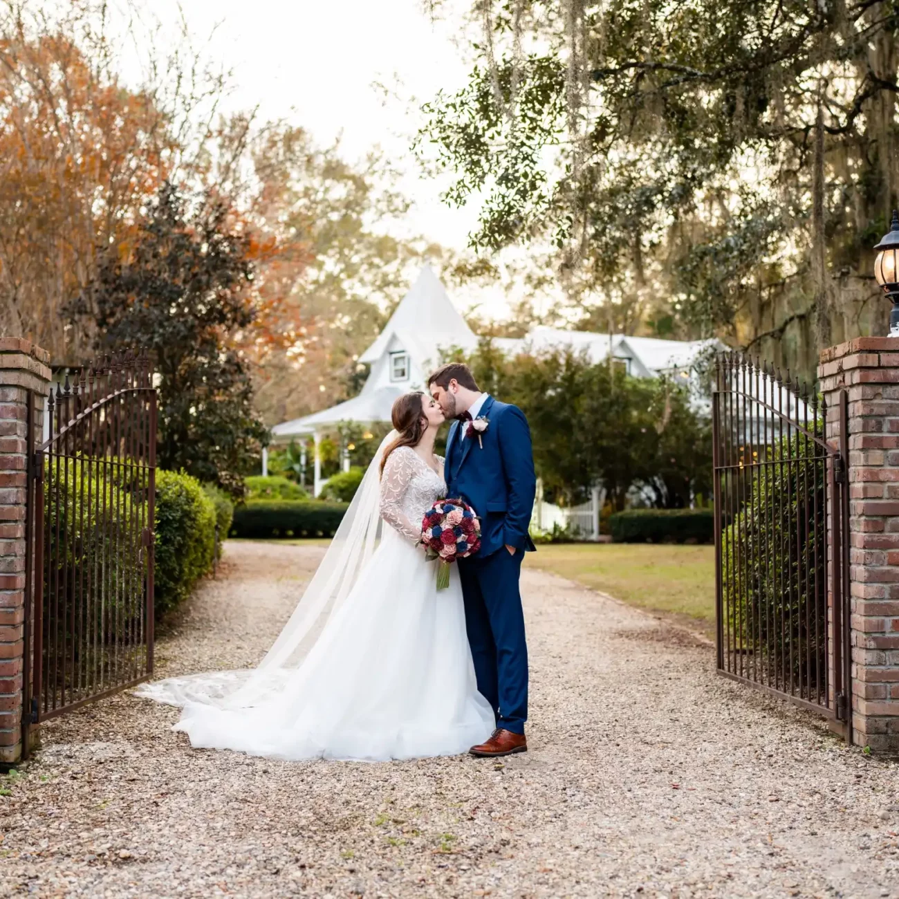 husband and wife rustic blue suit white veil gravel path between stone gateways