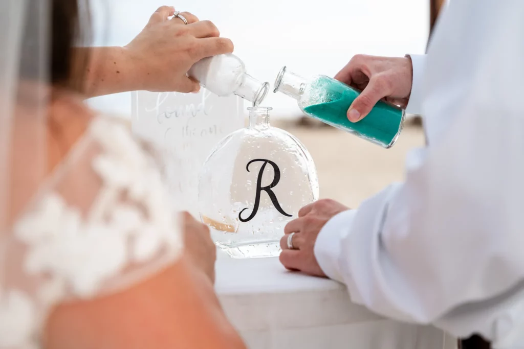 Panama City Beach Wedding Photographer 6 Chad & Rena adding colored sand to a glass bottle with the letter R on it to symbolize their new marriage