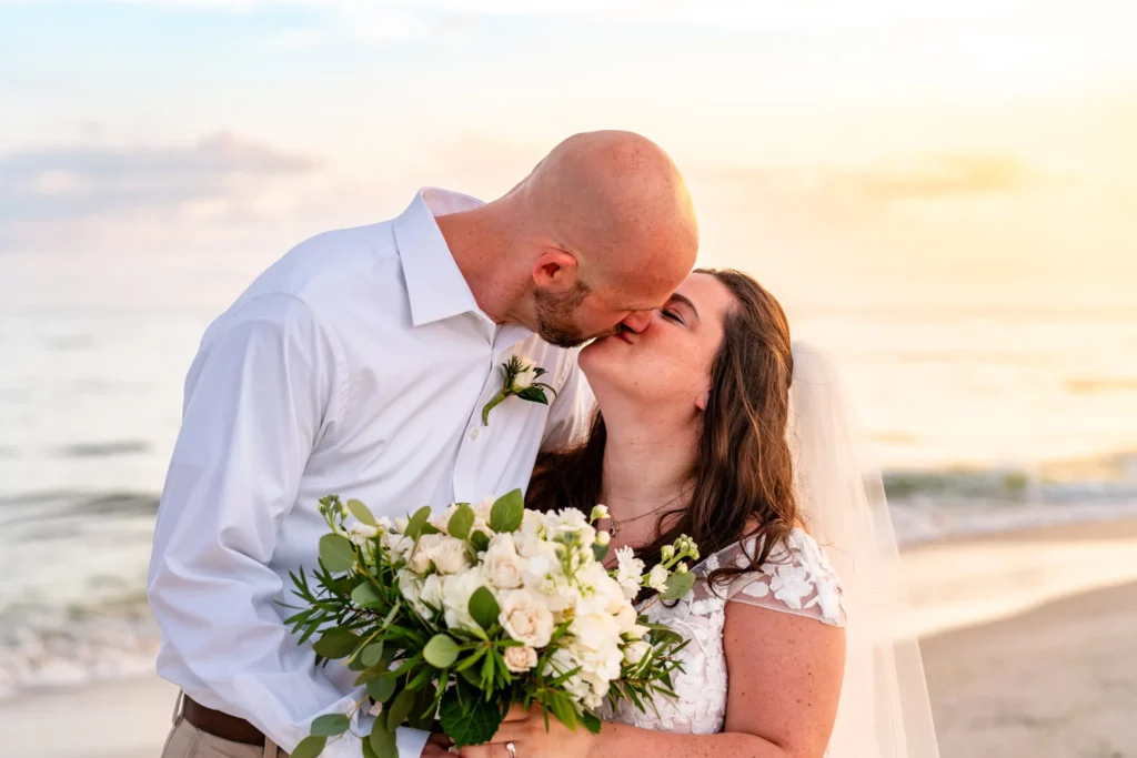 Panama City Beach Wedding Photographer 3 Chad & Rena kissing on orange beach after getting married, Rena is holding a beautiful white rose bouquet