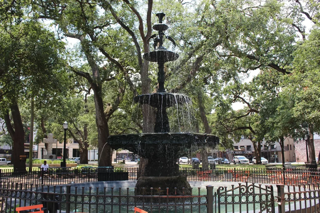 19 Best Engagement Photo Spots in Mobile, Alabama (With Parking, Timing & Real Session Examples) 8 Mardi Gras park fountain mobile, al A tiered black fountain sprays water in a shady city park, surrounded by mature oak trees, iron fencing, benches, and downtown buildings.