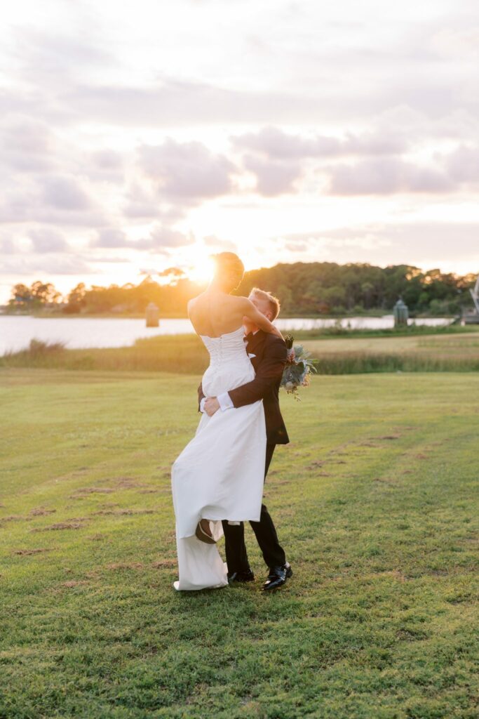Jake & Lauren's Hurlburt Field Wedding on Santa Rosa Sound 1 Groom lifts his bride at sunset on the grass beside Santa Rosa Sound at Hurlburt Field