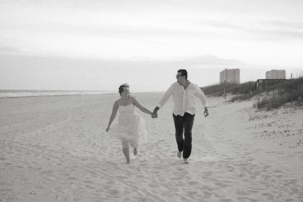 Andrew & Katie's Pensacola Beach Engagement Photos and Film 8 Black and white photo of Andrew and Katie running hand in hand on the beach