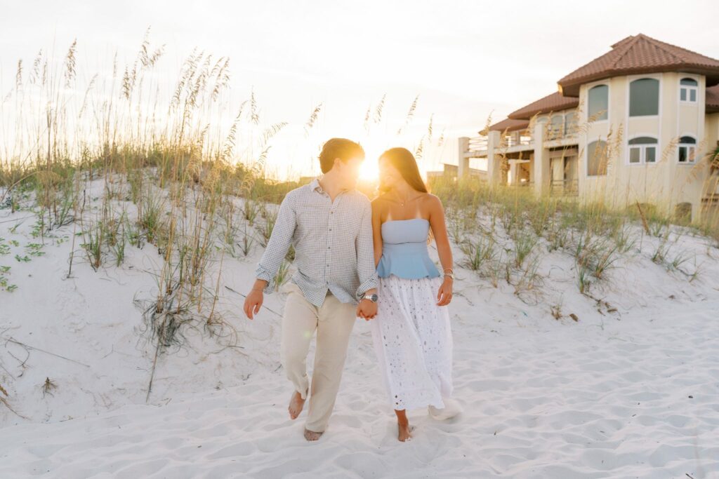 Hayes & Mallory's Surprise Proposal on Pensacola Beach 9 Hayes and Mallory walk through the sea oats with beach houses behind them