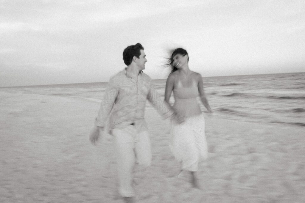 Hayes & Mallory's Surprise Proposal on Pensacola Beach 11 Black and white photo of Hayes and Mallory running along the water's edge