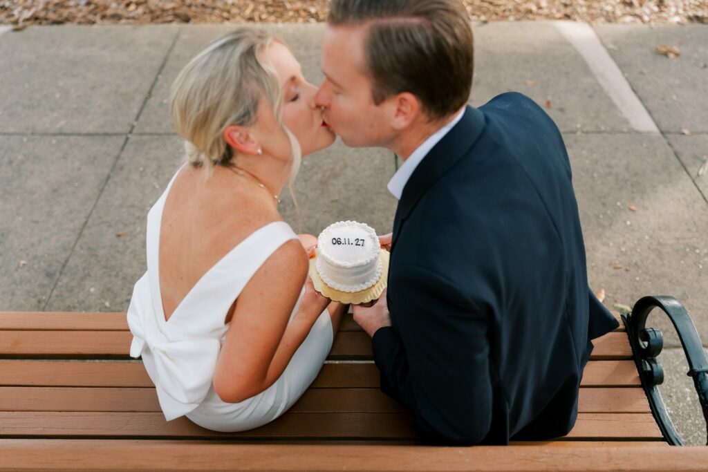 Sean and Brooklin kiss on a park bench holding a small cake