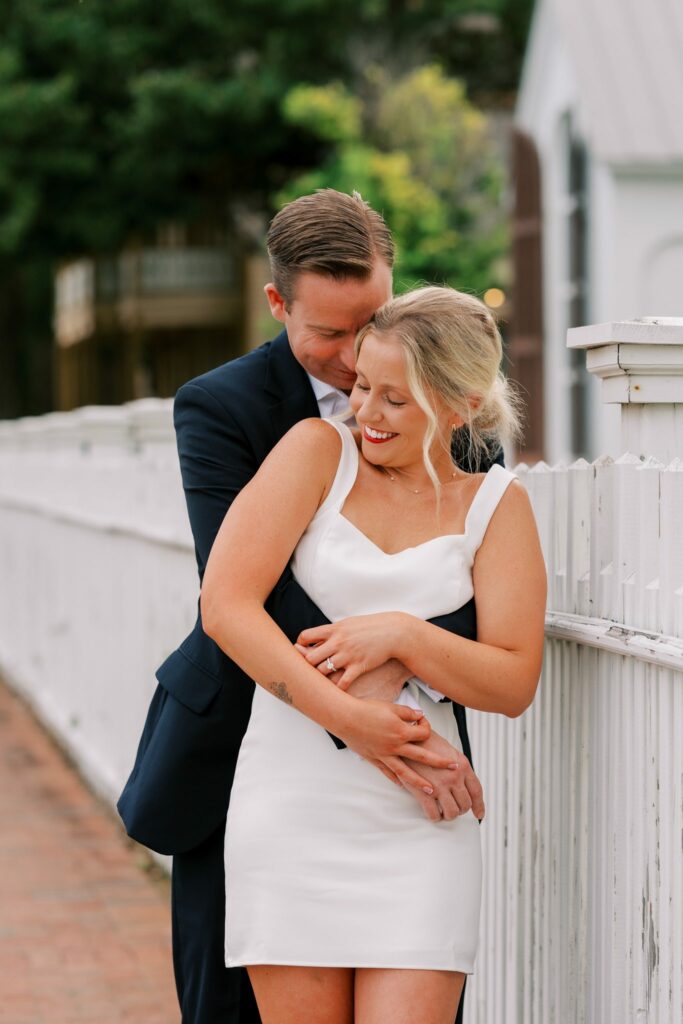 Sean hugs Brooklin from behind beside a white picket fence in the historic district