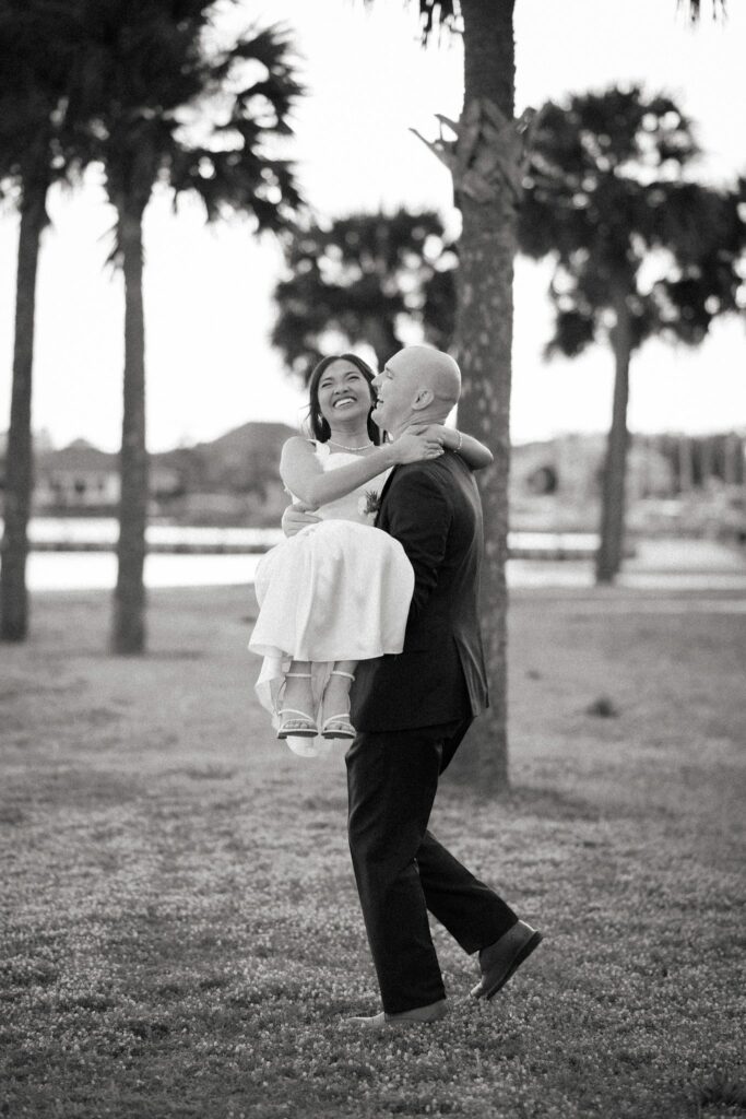 Bret & Ella's Spring Warehouse Wedding in Pensacola 7 Black and white photo of Bret lifting Ella under the palm trees
