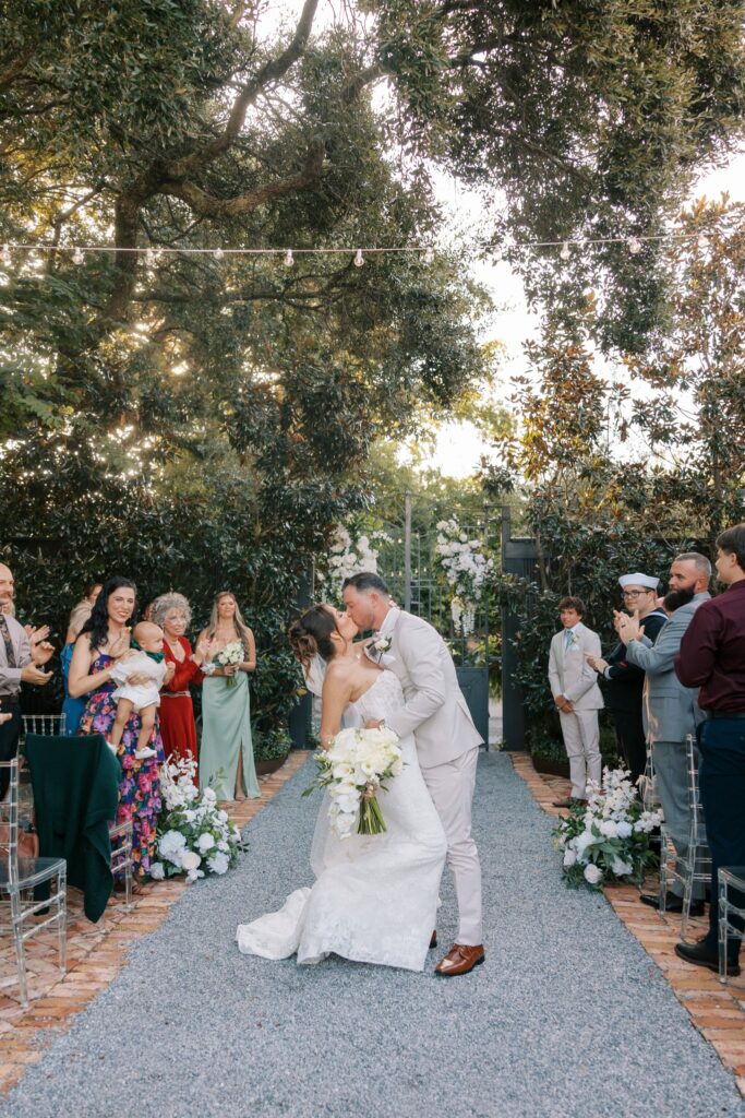 Nick & Amanda's Supposey Warehouse Wedding in Pensacola 1 Nick and Amanda kiss at the end of the garden ceremony aisle at Supposey Warehouse and Gardens in Pensacola