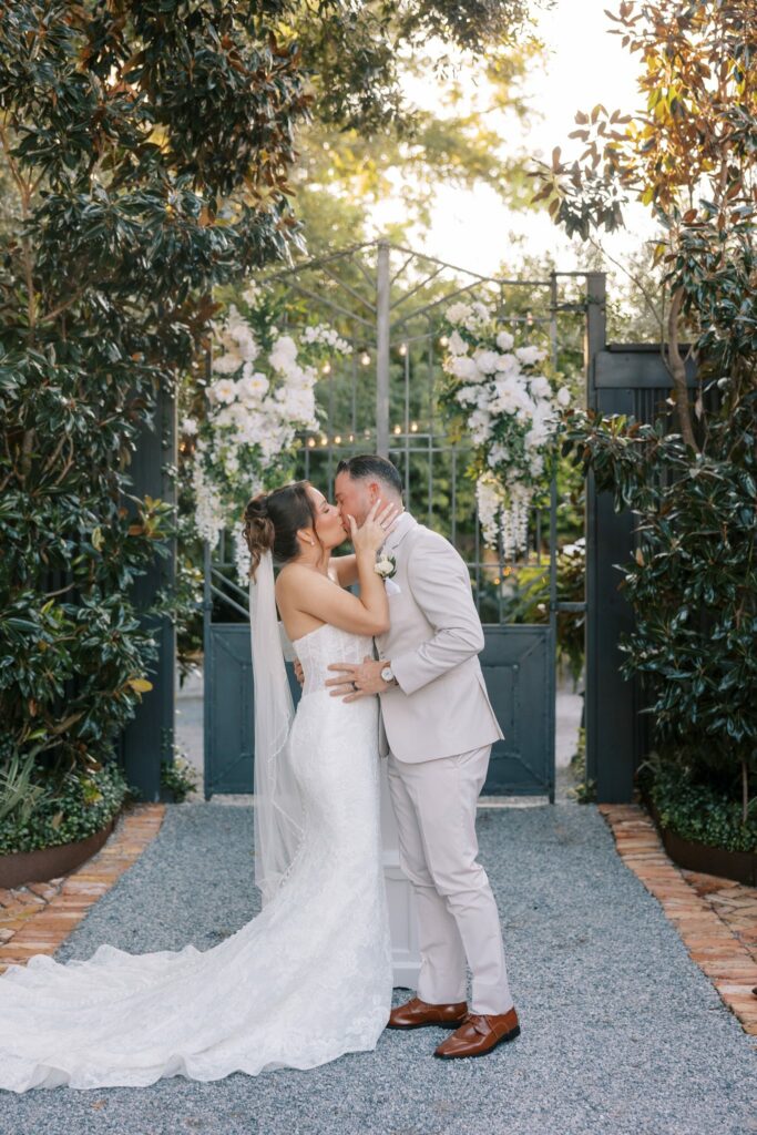 Nick & Amanda's Supposey Warehouse Wedding in Pensacola 4 Nick and Amanda kiss in front of the black iron gate at the end of the Supposey garden aisle