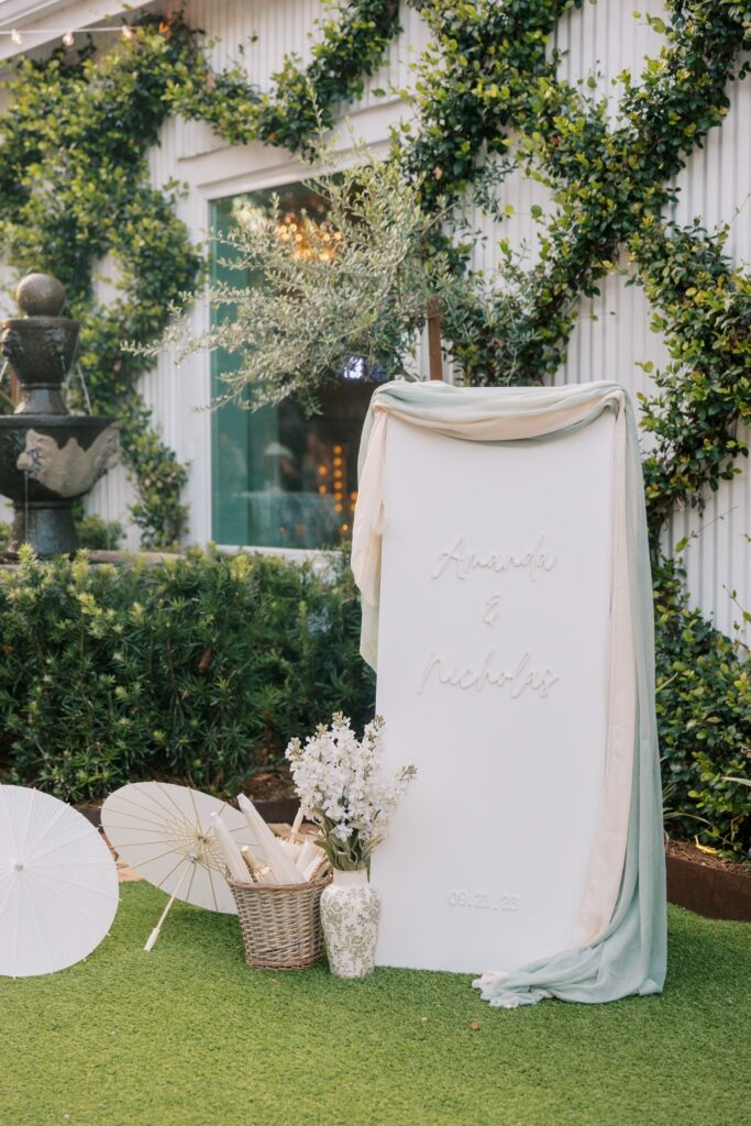 Nick & Amanda's Supposey Warehouse Wedding in Pensacola 5 Wedding welcome sign and white parasols against the ivy-covered wall at Supposey in Pensacola
