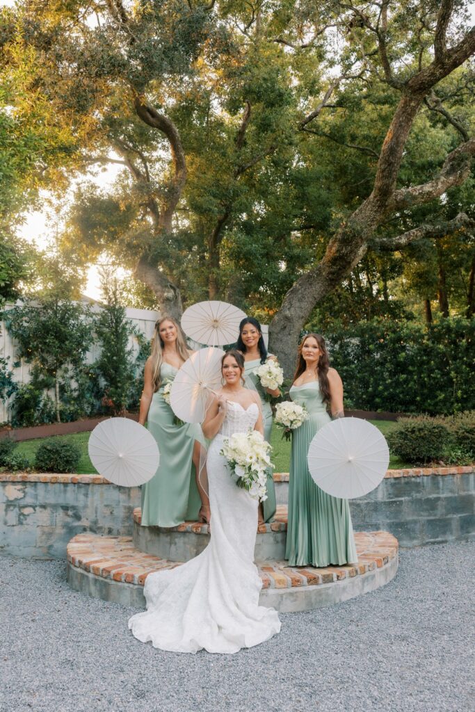 Nick & Amanda's Supposey Warehouse Wedding in Pensacola 6 Amanda with her bridesmaids in sage green holding white parasols on the round brick steps at Supposey