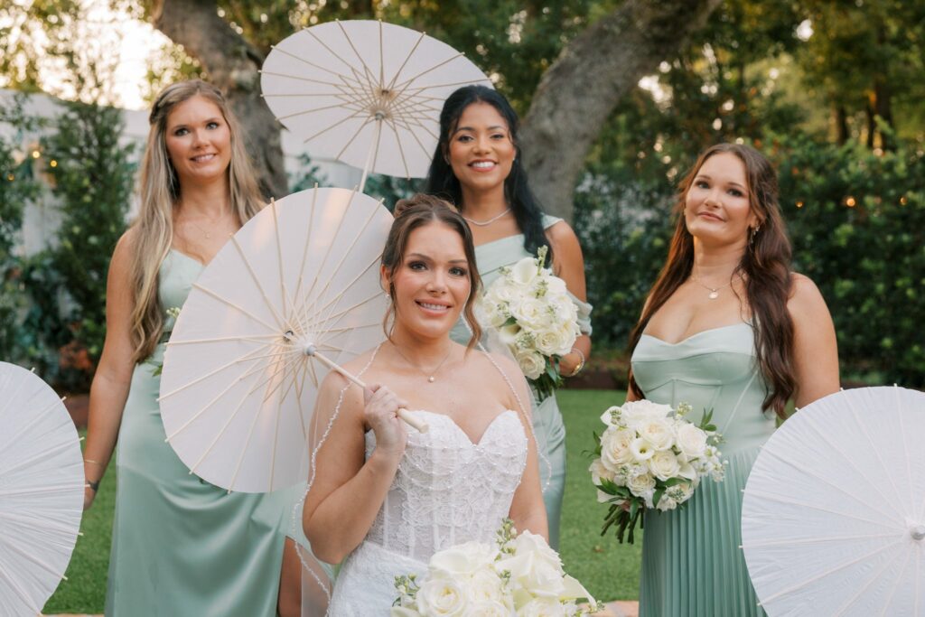 Nick & Amanda's Supposey Warehouse Wedding in Pensacola 7 Bride and bridesmaids with white paper parasols in the Supposey side garden
