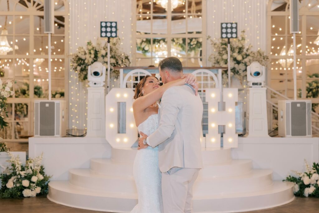 Nick & Amanda's Supposey Warehouse Wedding in Pensacola 10 First dance in front of giant marquee initials on the stage of the white Supposey ballroom