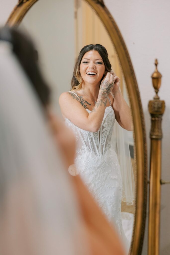 Josh & Haley's Hidden Oak Farm Wedding in Milton, FL 5 Haley laughing at a gold oval mirror in her wedding gown and veil before her Hidden Oak Farm wedding in Milton, FL