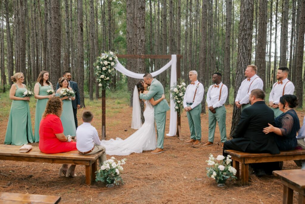 Josh & Haley's Hidden Oak Farm Wedding in Milton, FL 10 Josh and Haley kiss at the wooden arch while the wedding party and guests look on at Hidden Oak Farm