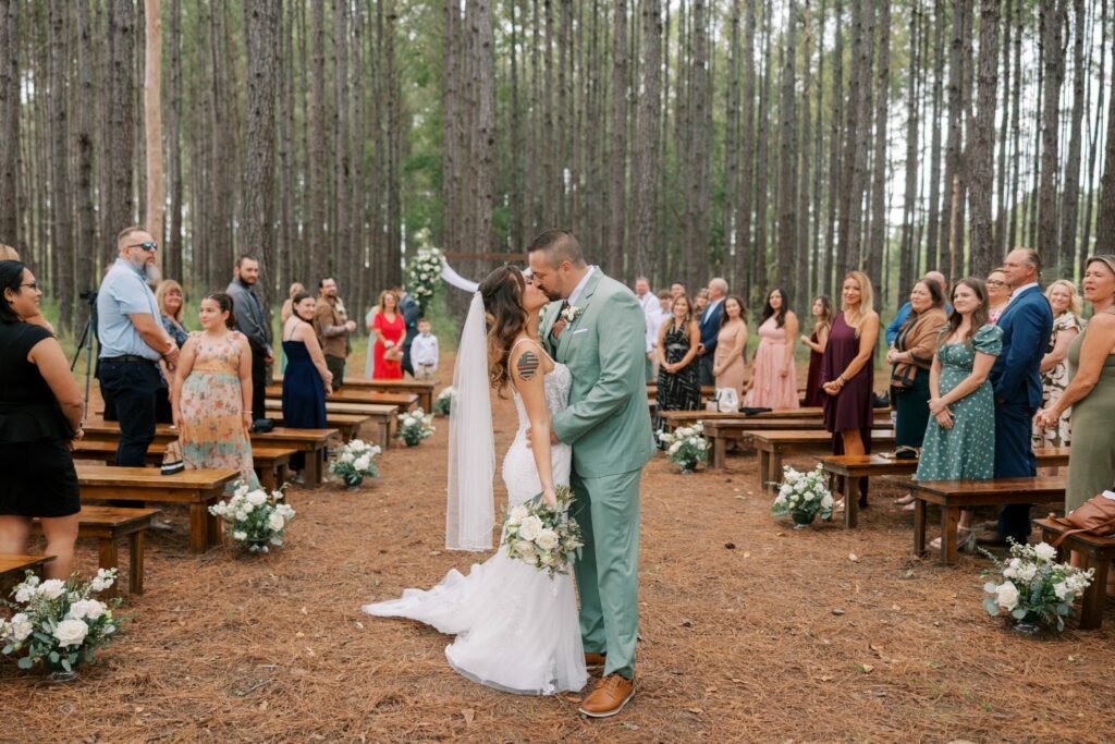 Josh & Haley's Hidden Oak Farm Wedding in Milton, FL 11 Josh and Haley's first kiss at their Hidden Oak Farm ceremony with guests standing along the benches