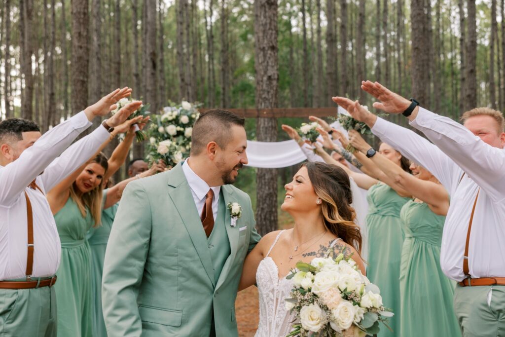 Josh & Haley's Hidden Oak Farm Wedding in Milton, FL 13 Josh and Haley smile at each other as the wedding party makes a hand tunnel at Hidden Oak Farm in Milton, FL