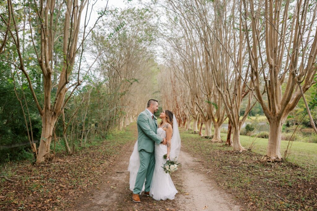 Josh & Haley's Hidden Oak Farm Wedding in Milton, FL 17 Josh and Haley stand together on a tree-lined dirt lane at Hidden Oak Farm in Milton, FL