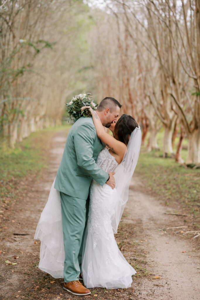 Josh & Haley's Hidden Oak Farm Wedding in Milton, FL 18 Josh in a sage green suit holds Haley in an embrace on the tree-lined lane at Hidden Oak Farm