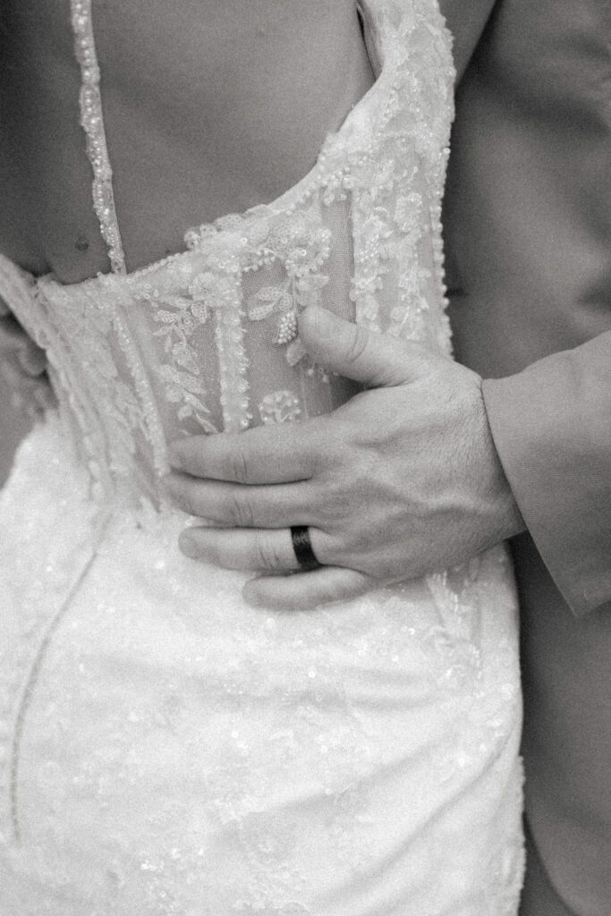 Josh & Haley's Hidden Oak Farm Wedding in Milton, FL 20 Black and white detail of Josh's hand on the back of Haley's lace wedding gown, with his wedding band visible