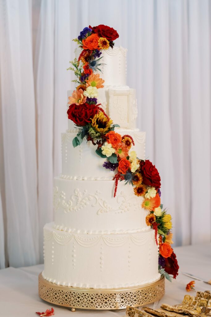 Jacob & Angelina's Holland Farms Wedding 15 Tall white tiered wedding cake by Ceejays Sweets with cascading red, orange and yellow flowers at Holland Farms