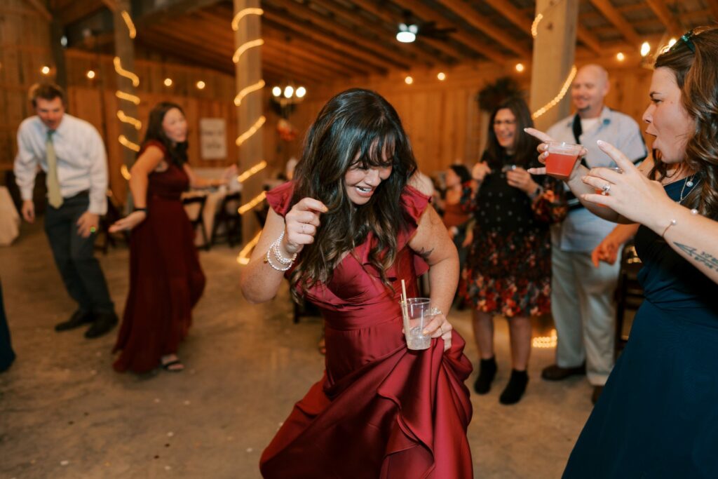 Jacob & Angelina's Holland Farms Wedding 18 Guest in a burgundy dress dancing in the string-lit barn at Jacob and Angelina's Holland Farms reception