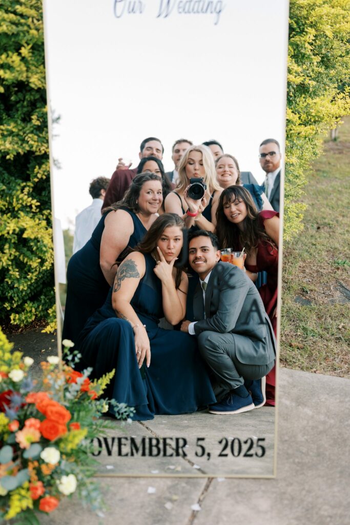 Jacob & Angelina's Holland Farms Wedding 20 Wedding party in navy, gray and burgundy posing in a full-length mirror sign that reads Our Wedding, with the photographer visible in the reflection