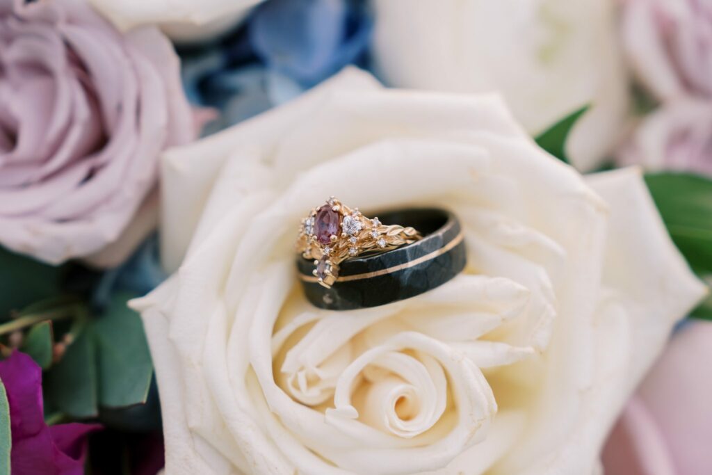 Brandon & Victoria's Laurel Hill Farm Wedding 19 Wedding rings resting on a white rose with lavender roses behind, from a Hummingbird Florals bouquet