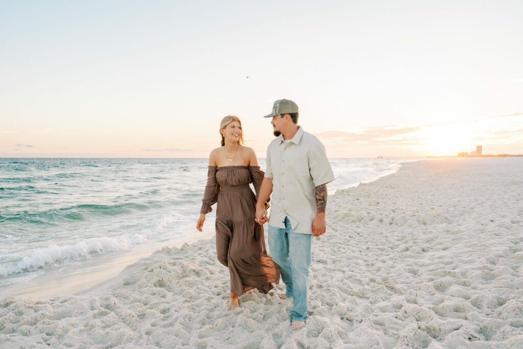 Avery & Hannah's Orange Beach Proposal 4 Avery and Hannah hold hands and walk along the Orange Beach shoreline at sunset