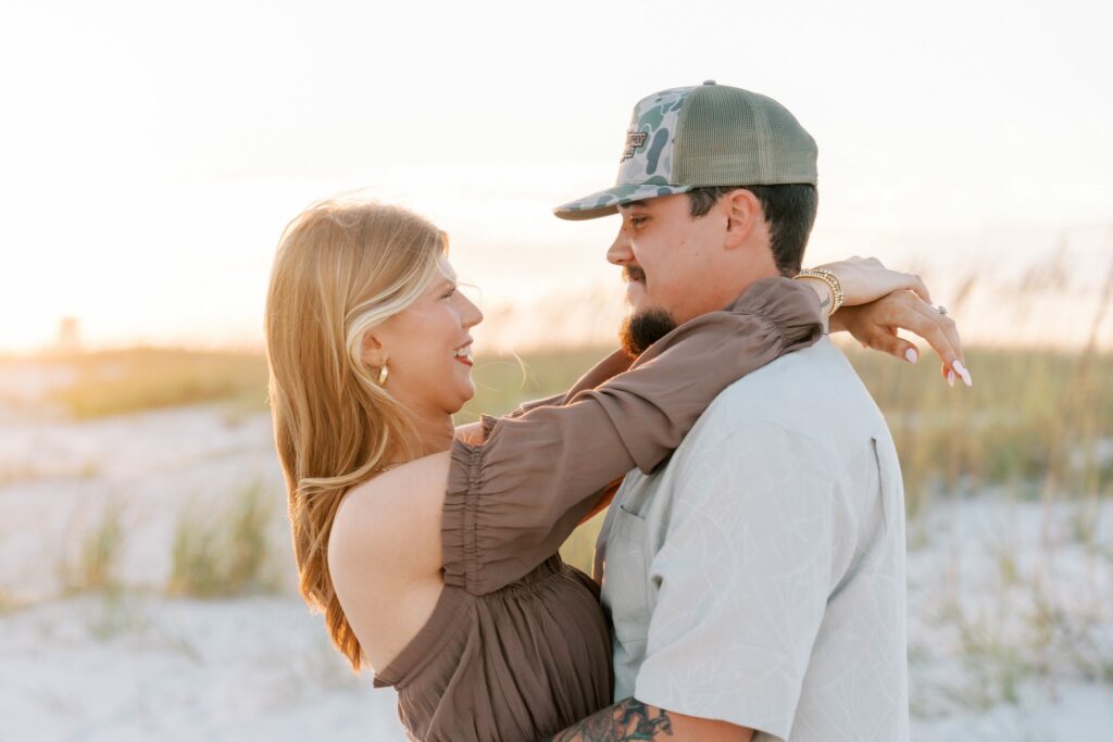 Avery & Hannah's Orange Beach Proposal 5 Hannah laughs and hugs Avery in front of sea oats during their Orange Beach engagement photos