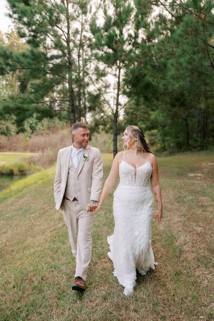 Anthony & Renee's Wedding at The Venue at Hidden Falls 11 Anthony and Renee holding hands walking across the lawn by the pond at Hidden Falls in Flomaton, AL