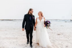 Beautiful Wedding At Navarre Beach Wedding House 19 a man and woman holding hands and smiling on the beach in suit and bridal dress at Navarre Beach Wedding House