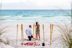 Bryan’s Surprising and Memorable Proposal to Cheree Miramar Beach, FL 4 man on one knee in front of woman on beach, tiki torches in frame, proposing to his soon to be fiance on Miramar Beach, FL captured by KDH Weddings