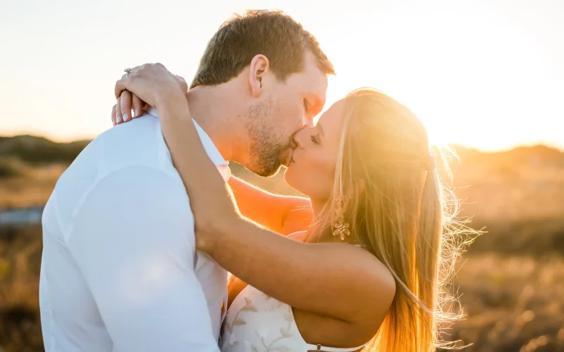 Ryan and Kinsie kissing in the Fort Pickens dunes, backlit by the setting sun over the sea oats