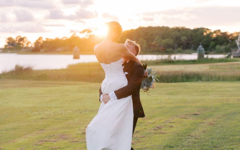 Groom lifts his bride at sunset on the grass beside Santa Rosa Sound at Hurlburt Field