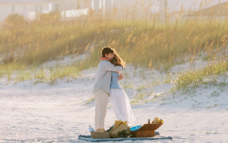 Hayes and Mallory embrace right after his surprise proposal beside a picnic setup on Pensacola Beach